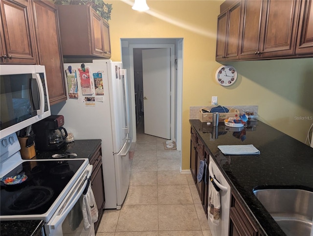 kitchen with white appliances, light tile patterned flooring, and dark stone counters