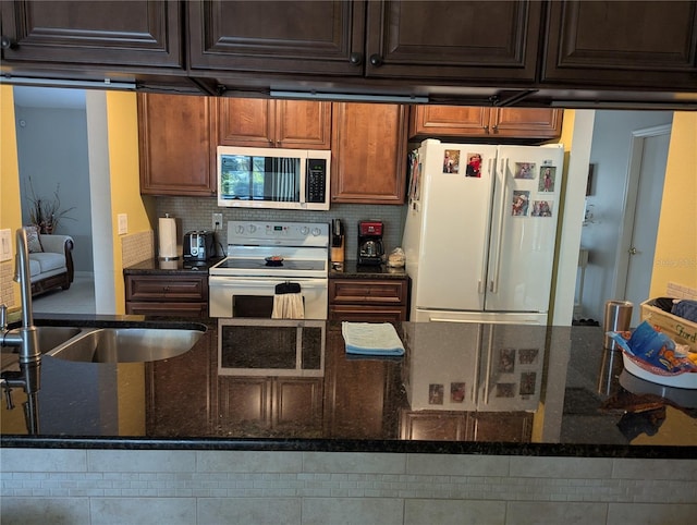 kitchen with white appliances, dark stone counters, backsplash, and a sink