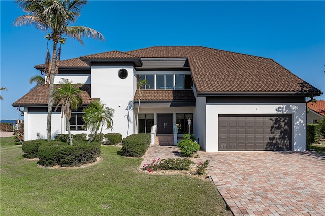 view of front facade featuring stucco siding, a front lawn, a garage, a tiled roof, and decorative driveway