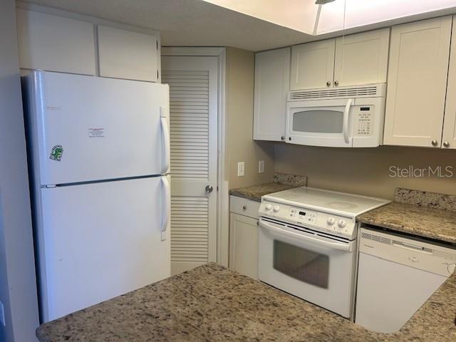 kitchen featuring white appliances, white cabinets, and light stone countertops