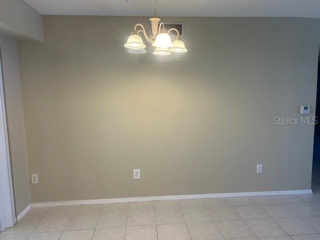 empty room featuring a notable chandelier, visible vents, baseboards, and light tile patterned floors