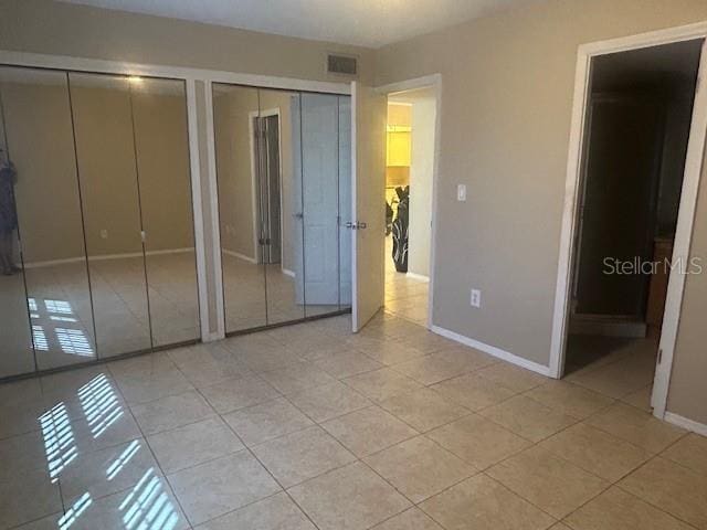 unfurnished bedroom featuring light tile patterned floors, visible vents, baseboards, ensuite bath, and multiple closets