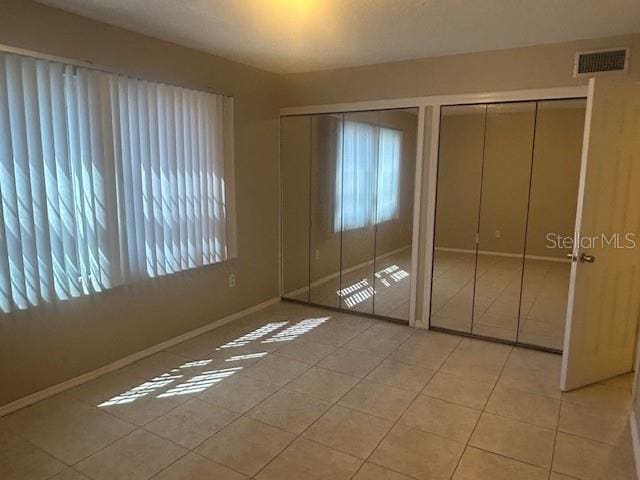 unfurnished bedroom with visible vents, baseboards, two closets, and light tile patterned flooring