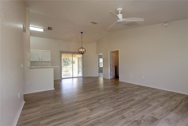 empty room featuring visible vents, ceiling fan with notable chandelier, light wood-type flooring, and high vaulted ceiling