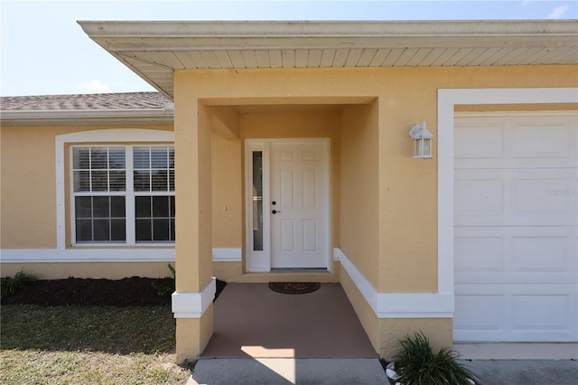 view of exterior entry with stucco siding, a garage, and roof with shingles