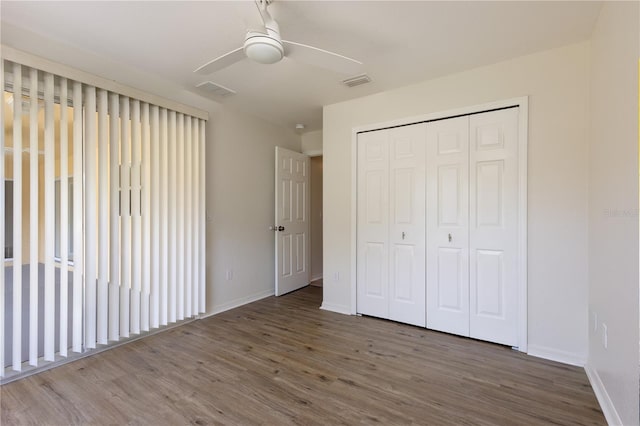 unfurnished bedroom with wood finished floors, visible vents, a closet, and baseboards