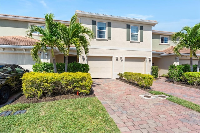 view of front facade with stucco siding, an attached garage, a tile roof, and decorative driveway