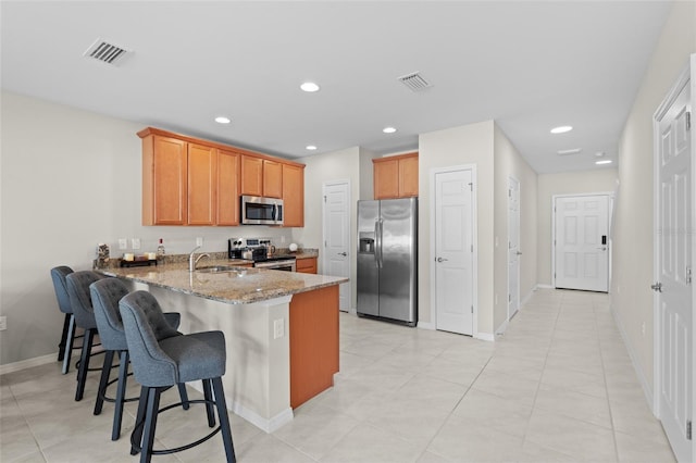 kitchen with visible vents, a peninsula, stainless steel appliances, and light stone countertops