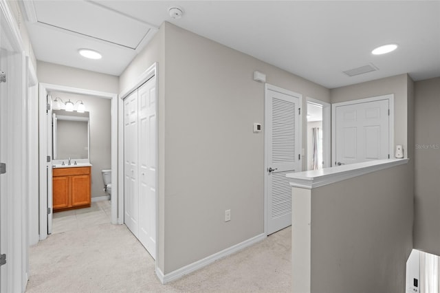 hall featuring baseboards, light colored carpet, and attic access