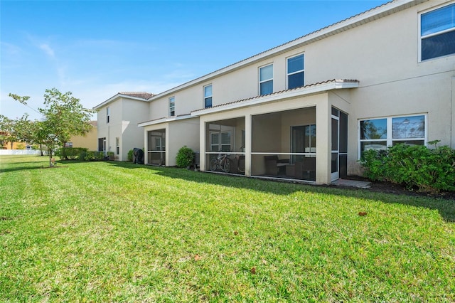 rear view of property featuring a lawn, a sunroom, and stucco siding