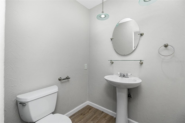 half bath with a sink, baseboards, toilet, and wood finished floors