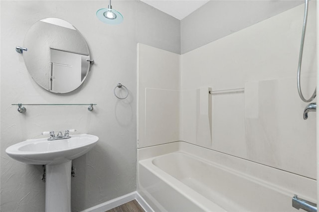 bathroom with baseboards, wood finished floors, and washtub / shower combination