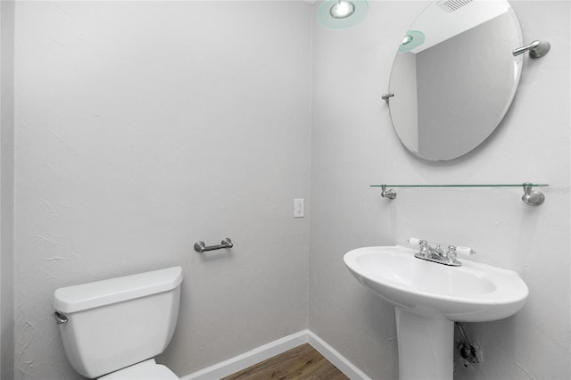 half bath with a sink, baseboards, toilet, and wood finished floors