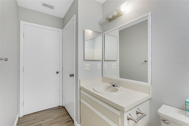 half bath with vanity, toilet, wood finished floors, and visible vents