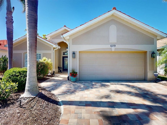 ranch-style house featuring stucco siding, decorative driveway, and a garage