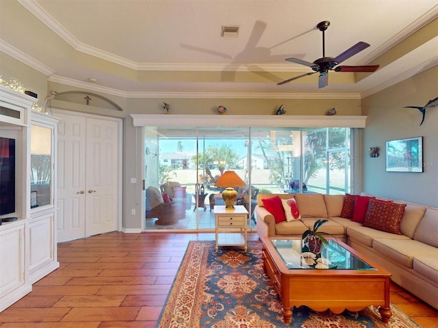 living area featuring wood finished floors, visible vents, a tray ceiling, ceiling fan, and crown molding