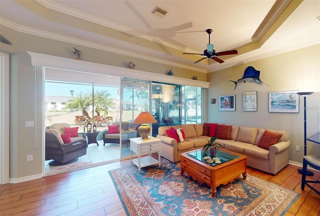 living room featuring hardwood / wood-style floors, a tray ceiling, visible vents, and ornamental molding