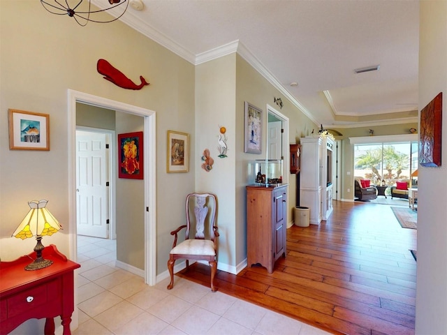 corridor with crown molding, baseboards, visible vents, and light wood finished floors