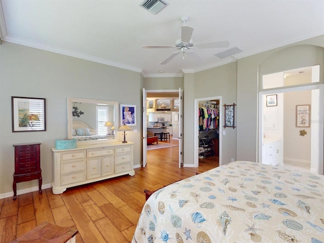 bedroom featuring visible vents, a walk in closet, baseboards, ornamental molding, and light wood-style flooring