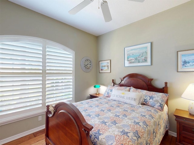 bedroom featuring baseboards, multiple windows, wood finished floors, and a ceiling fan