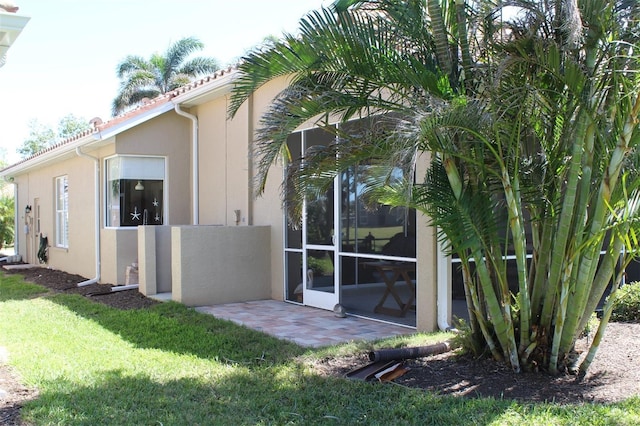 view of home's exterior featuring stucco siding, a patio, a yard, and a sunroom