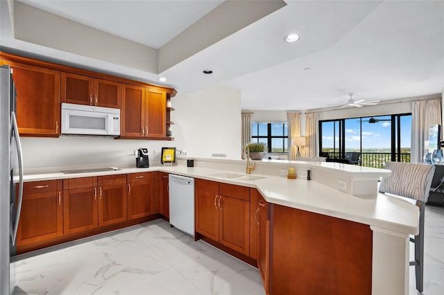 kitchen with a breakfast bar, a peninsula, marble finish floor, white appliances, and a sink