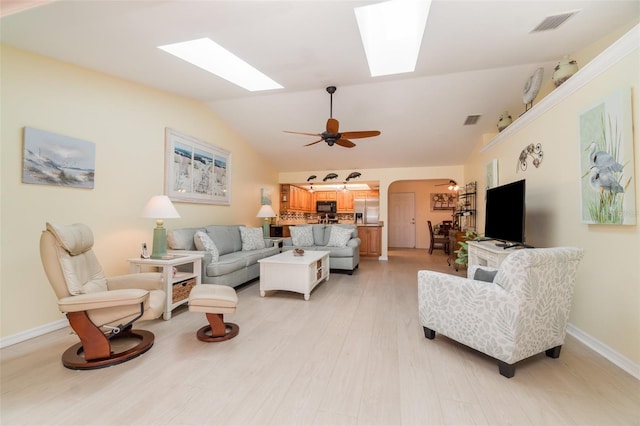 living room with a ceiling fan, baseboards, light wood finished floors, arched walkways, and lofted ceiling with skylight