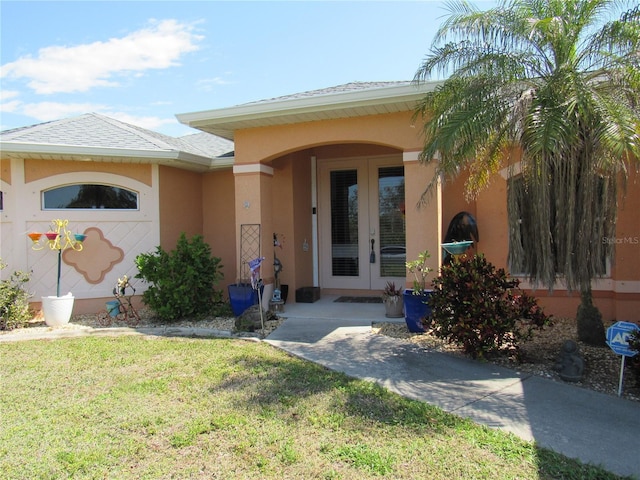 property entrance featuring a shingled roof, french doors, a lawn, and stucco siding