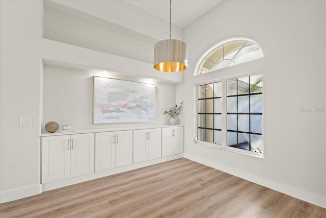 unfurnished dining area featuring baseboards and light wood finished floors