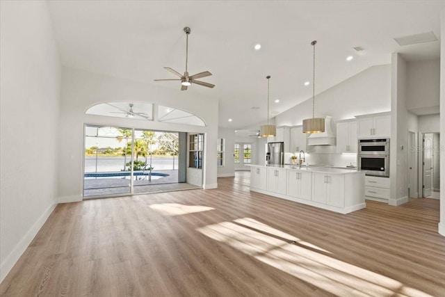 unfurnished living room featuring a ceiling fan, baseboards, high vaulted ceiling, a sink, and light wood-type flooring