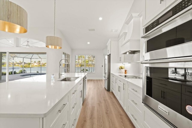 kitchen with light wood finished floors, stainless steel appliances, a sink, pendant lighting, and white cabinetry