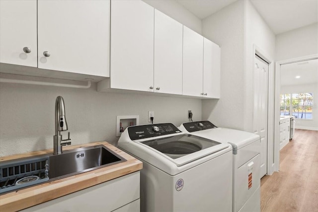 laundry room with a sink, cabinet space, light wood-style floors, and separate washer and dryer