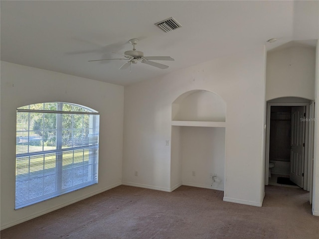 spare room featuring visible vents, built in shelves, a ceiling fan, baseboards, and light colored carpet