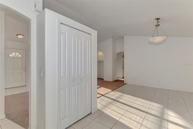 interior space featuring arched walkways, light tile patterned floors, light carpet, and lofted ceiling