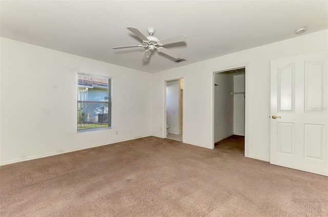 unfurnished bedroom with a ceiling fan, visible vents, a closet, light carpet, and a walk in closet