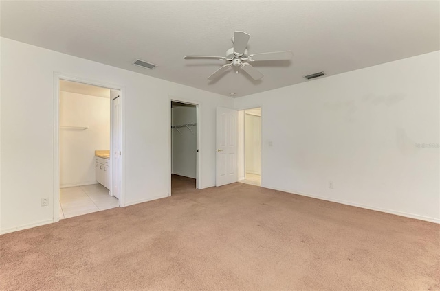 unfurnished bedroom featuring a spacious closet, visible vents, light colored carpet, and connected bathroom