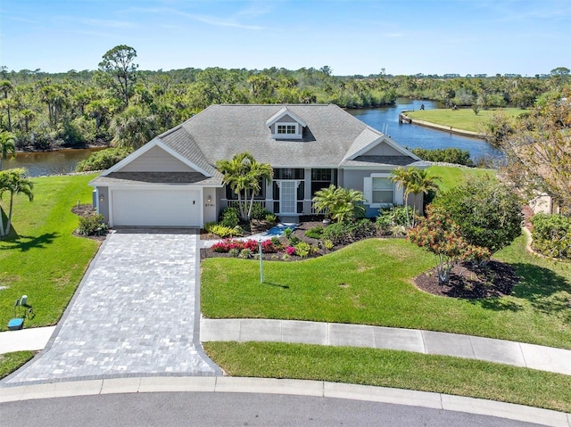 view of front of property with a water view, decorative driveway, a wooded view, a front yard, and a garage