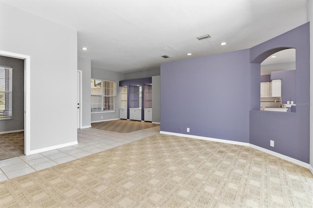 tiled empty room featuring arched walkways, visible vents, baseboards, and a sink