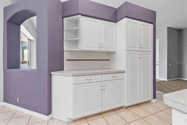 kitchen featuring decorative backsplash, light countertops, light tile patterned flooring, and white cabinetry