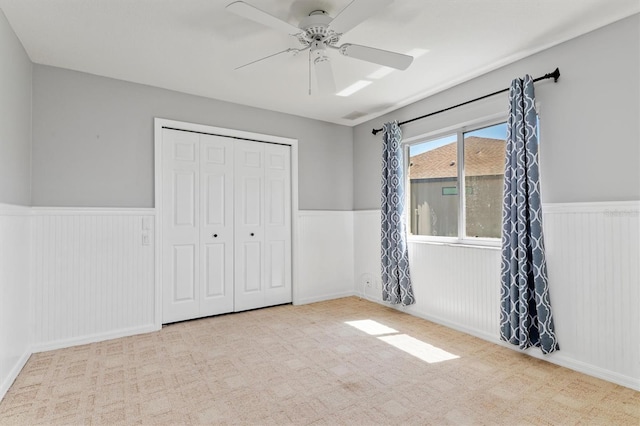 unfurnished bedroom with a closet, a wainscoted wall, and a ceiling fan