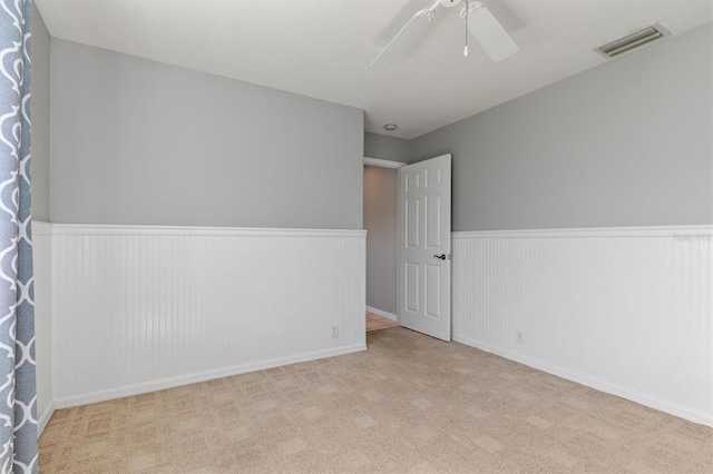 spare room with ceiling fan, visible vents, carpet, and a wainscoted wall