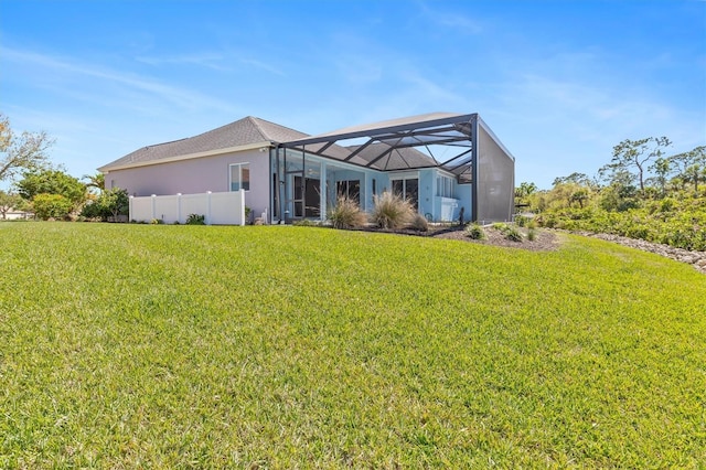 back of house featuring glass enclosure, a lawn, fence, and stucco siding