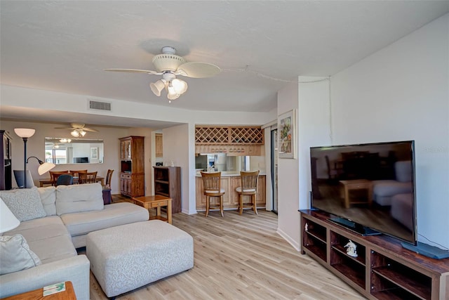 living room with a bar, light wood-style flooring, a ceiling fan, and visible vents