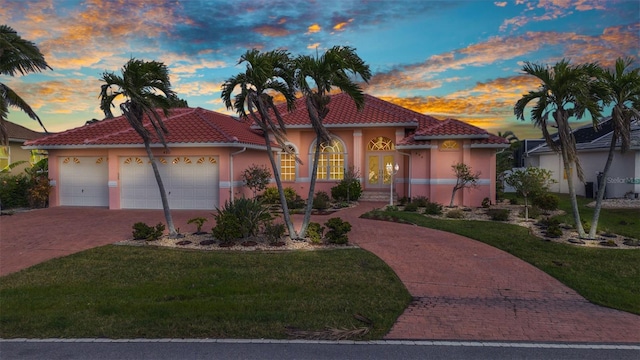 mediterranean / spanish house with stucco siding, a tile roof, decorative driveway, a yard, and a garage