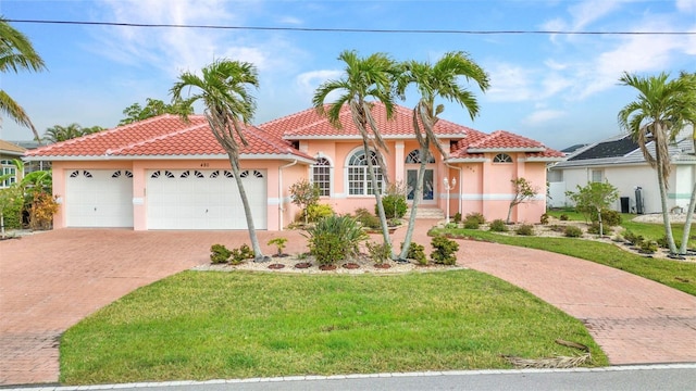 mediterranean / spanish home featuring a tile roof, decorative driveway, a front yard, and stucco siding