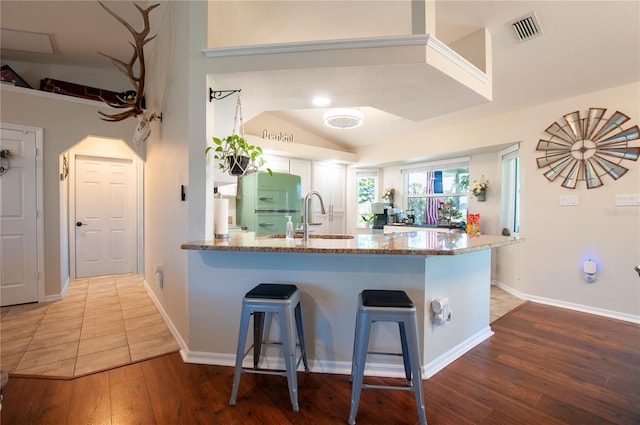 kitchen featuring visible vents, a breakfast bar, a sink, freestanding refrigerator, and a peninsula