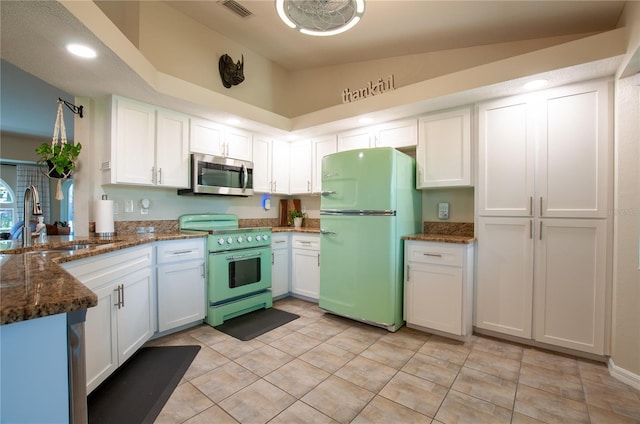 kitchen featuring a sink, dark stone countertops, stainless steel appliances, white cabinets, and vaulted ceiling