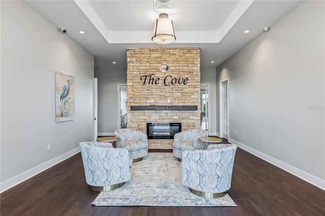 living area featuring a fireplace, a raised ceiling, wood finished floors, and baseboards