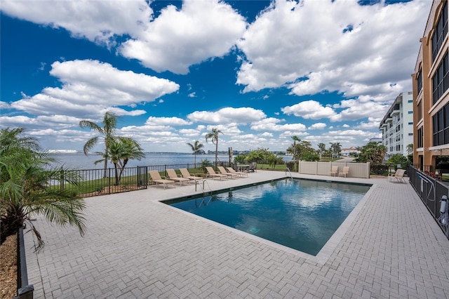 pool with a patio area, fence, and a water view