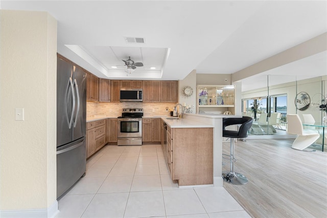 kitchen featuring a tray ceiling, a peninsula, a sink, stainless steel appliances, and a kitchen bar